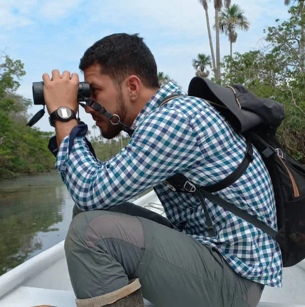 Integrante del equipo observando aves con binoculares junto al agua